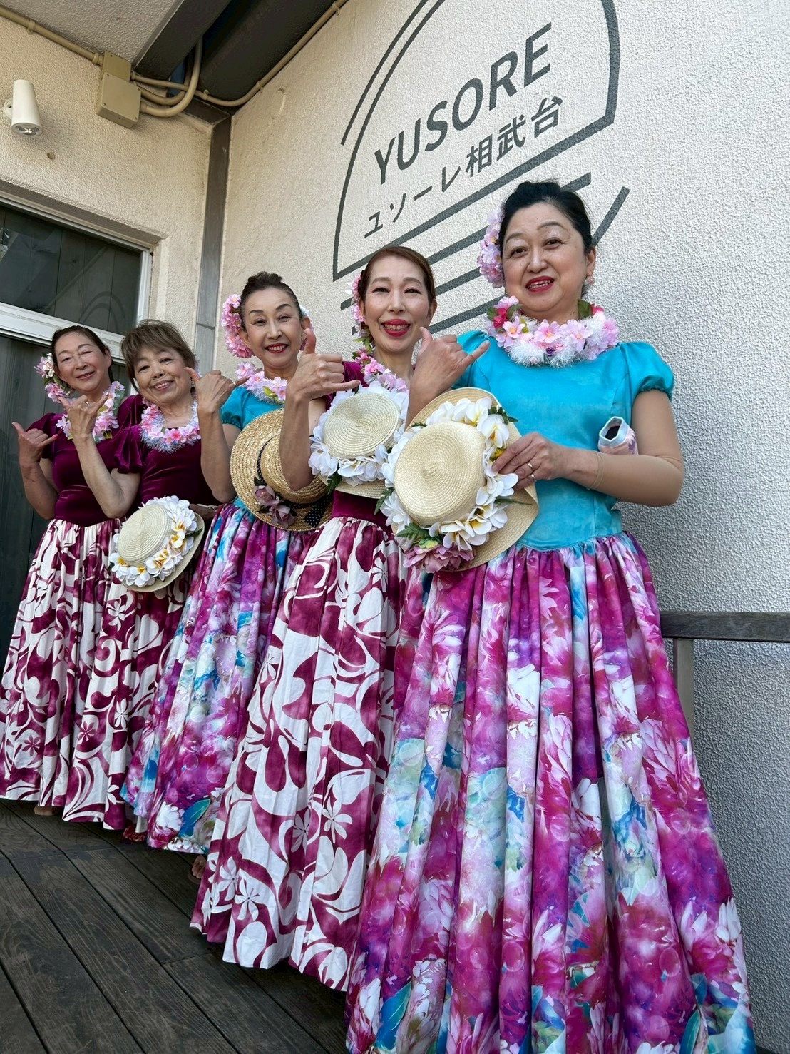 YUSOREの看板の前で、フラの衣装を着て笑う踊り手のみなさん