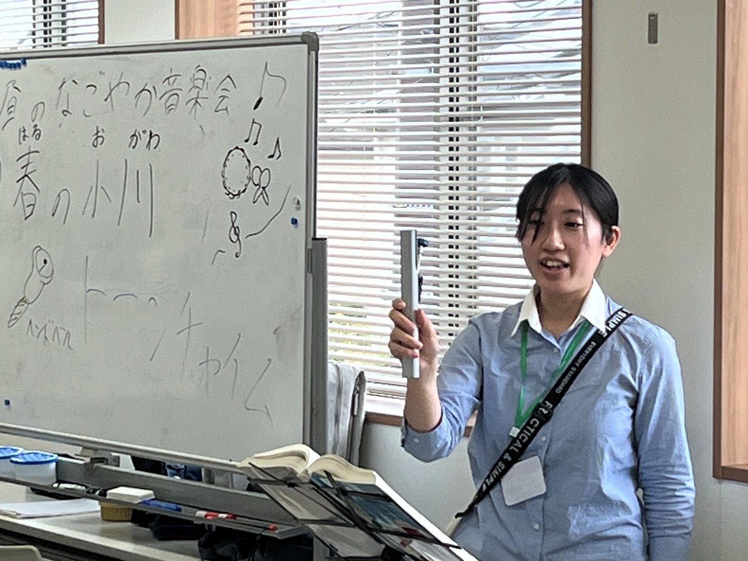 ホワイトボードの前で、トーンチャイムを持って笑うスタッフ